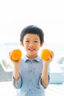 Mignon petit asiatique garçon tenue orange fruits — Photo de stock