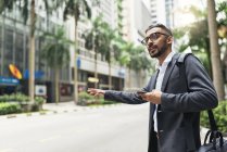 Young successful businessman using smartphone and catching cab — Stock Photo