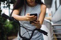Jeune asiatique femme avec vélo en utilisant smartphone — Photo de stock