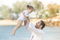 Счастливая кавказская семья на пляже, отец держит дочь — стоковое фото