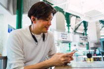 Молодий азіатський чоловік використовує смартфон у кафе — стокове фото