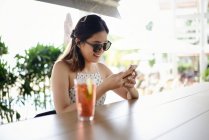 Молода приваблива азіатська жінка в сонцезахисних окулярах за допомогою смартфона — стокове фото
