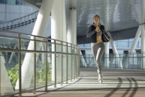 Uma jovem mulher asiática está correndo pela cidade de Singapura no início da manhã. Ela passa por uma seção de arquitetura de aço e vidro . — Fotografia de Stock