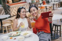 Joven asiático mujeres amigos tomando selfie en comida tribunal - foto de stock