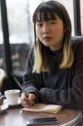 Joven atractivo casual asiático mujer escritura notas en café - foto de stock