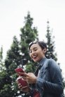 Young Singaporean Malay lady using her phone with trees as the background. — Stock Photo