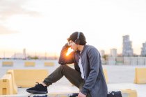 Joven asiático millennial hombre en auriculares disfrutando de la puesta del sol - foto de stock