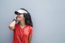 Jovem asiático desportivo mulher usando fones de ouvido contra cinza parede — Fotografia de Stock
