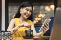 Щаслива молода азіатська жінка змішує каву і використовує смартфон — стокове фото