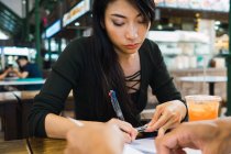 Jeune asiatique femme écriture quelque chose à table — Photo de stock