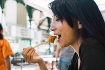 Young asian woman eating food with chopsticks — Stock Photo