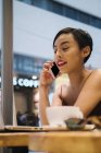 Mezzo ritratto della giovane malese di Singapore che usa il suo telefono in un caffè mentre lavora
. — Foto stock