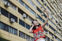 Asiático turista mulher tomando selfie contra casa durante o dia — Fotografia de Stock