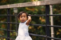 Cute little girl standing beside fence in park — Stock Photo
