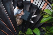 Joven atractivo asiático mujer sentado en escaleras con laptop - foto de stock