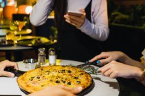 Обрезанный образ друзей резки пиццы в удобном баре — стоковое фото