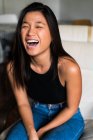 Jovem atraente asiático mulher sentado no poltrona e rindo — Fotografia de Stock