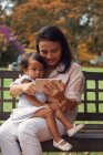 Lindo asiático madre y hija usando smartphone en banco - foto de stock