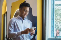 Young asian man using phone in creative modern office — Stock Photo