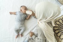 Asian muslim mother feeding milk to her baby on bed — Stock Photo