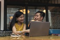 Happy young asian couple using laptop in cafe — Stock Photo