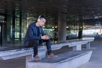 Молодий азіатський чоловік використовує гарнітуру та смартфон у місті — стокове фото