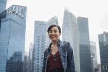 Joven dama singapurense sonriendo a la cámara y posando con rascacielos en Singapur . - foto de stock