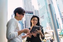 Joven asiático pareja compartir tableta en la ciudad - foto de stock