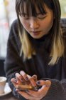 Молода приваблива випадкова азіатська жінка використовує смартфон у кафе — стокове фото