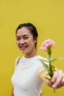 Молода приваблива азіатська жінка тримає рожеву квітку, жовтий фон — стокове фото