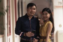 Glückliches junges asiatisches Paar, das sich umarmt und Smartphone benutzt — Stockfoto
