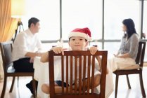 Happy asian family at christmas holidays, boy sitting on chair in santa hat — Stock Photo