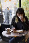 Young attractive casual asian woman drinking coffee and writing notes in cafe — Stock Photo