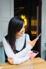 Giovane donna asiatica con smartphone in confortevole bar — Foto stock