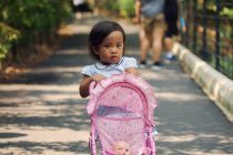 Little girl pushing baby carriage in park — Stock Photo
