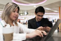Young asian couple of businesspeople using smartphone and laptop in airport — Stock Photo