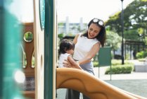 Joven madre con asiático hija en parque infantil - foto de stock