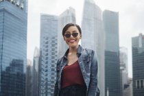 Giovane signora di Singapore che sorride alla telecamera e posa con i grattacieli a Singapore . — Foto stock