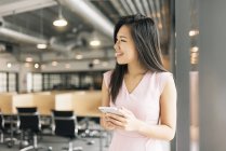 Junge erfolgreiche asiatische Geschäftsfrau mit Smartphone im modernen Büro — Stockfoto
