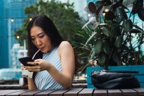 Jovem mulher asiática tendo bebida e usando smartphone — Fotografia de Stock