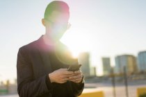 Junger asiatischer Mann mit Sonnenbrille benutzt Smartphone — Stockfoto