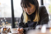 Молода приваблива випадкова азіатська жінка пише нотатки в кафе — стокове фото