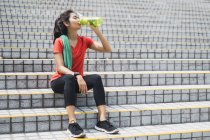 Junge asiatische sportliche Frau trinkt Wasser auf Treppen — Stockfoto