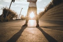 Imagem cortada de jovem asiático homem de pé contra o pôr do sol com os braços cruzados — Fotografia de Stock