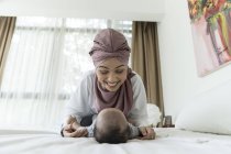 Asiático musulmán madre y bebé jugando en cama - foto de stock
