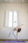 Joven asiático mujer haciendo estiramiento ejercicios contra ventana - foto de stock