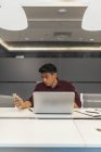 Junger asiatischer Geschäftsmann arbeitet mit Laptop und Smartphone im modernen Büro — Stockfoto