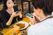 Молодая азиатская пара фотографирует еду в кафе — стоковое фото