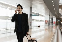 Молодий азіатський бізнесмен з багажем і смартфоном в аеропорту — стокове фото