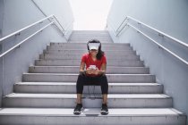 Giovane asiatica donna sportiva utilizzando cuffie e intelligente sulle scale — Foto stock